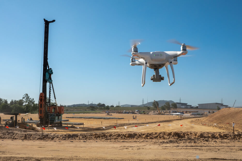 Dron monitoruje staveniště s vrtným strojem v pozadí pod modrou oblohou.